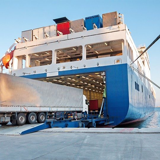Large cargo truck driving off the dock onto a giant cargo ship