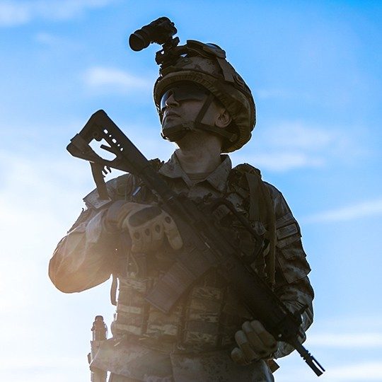 Military man dressed in a combat uniform, holding a weapon and looking up at the sky