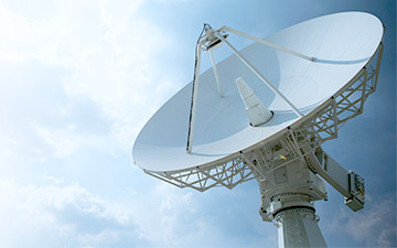 White ground station satellite communication antenna against a light blue sky with clouds