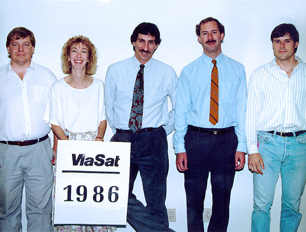 Founders Mark Dankberg, Steve Hart and Mark Miller plus two Viasat employees standing behind a sign that reads 'Viasat 1986'