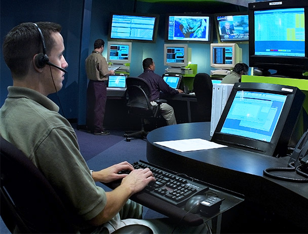 Three Viasat network operations employees monitoring data on computer and TV monitors
