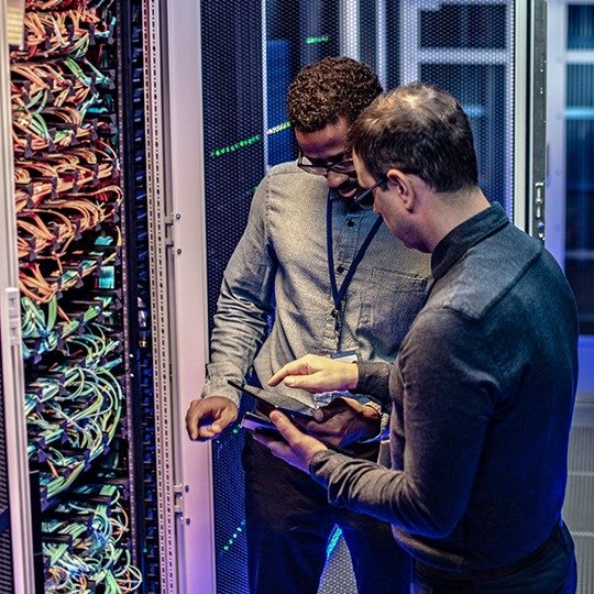 Two men in a server room discussing data protection and looking at a tablet