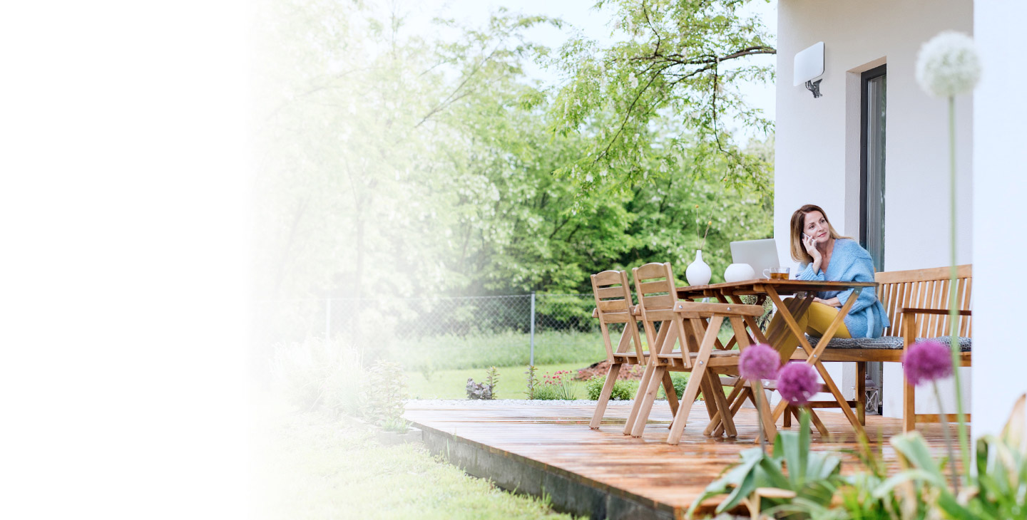 Woman sitting outside of her home at a wood table talking on the phone over fixed wireless