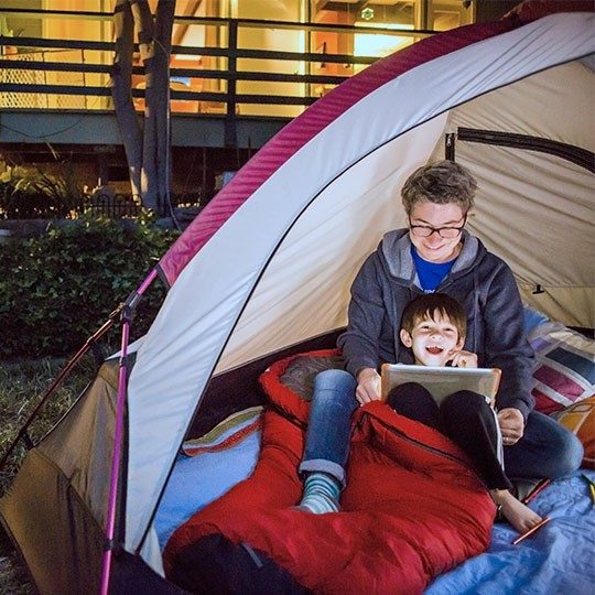 Two boys streaming content on a tablet over fixed wireless inside a tent in their backyard