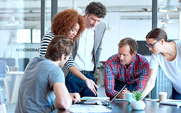 Five co-workers discussing space technology at a desk in front of a laptop