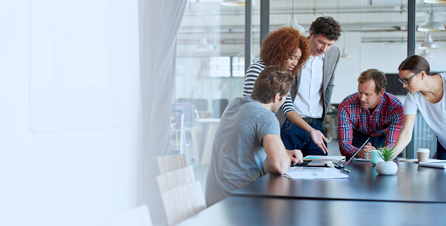 Five co-workers discussing custom antenna design at a large conference room desk