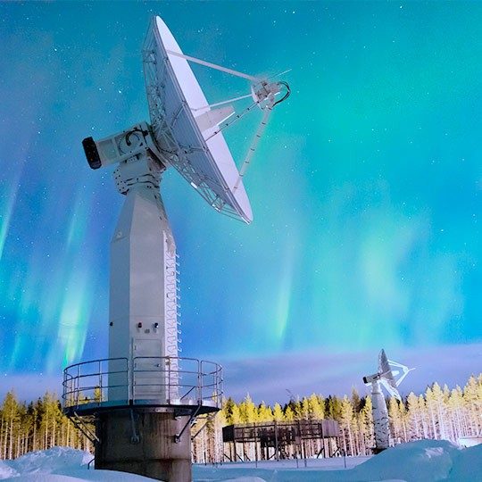 Two remote sensing antennas mounted in a snowy field pointed at a beautiful, blue streaky sky