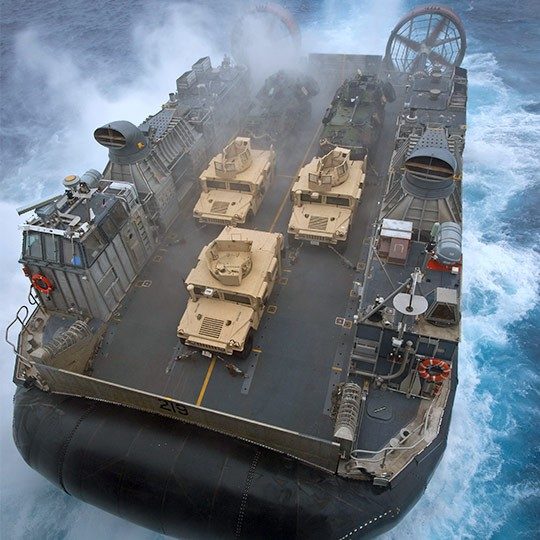 Aerial view of giant military hovercraft with mobile antennas at sea carrying three humvees 