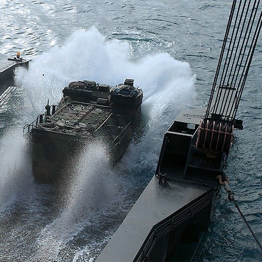 Military vehicle driving into the water off of a ship