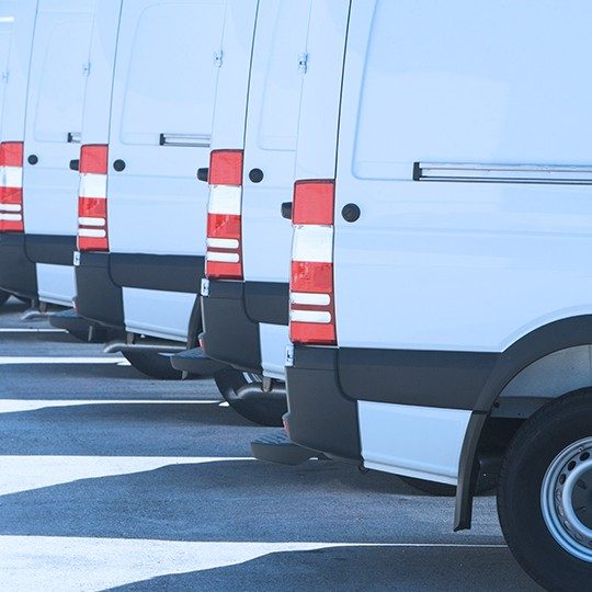Close-up image of the back tail lights of four white vans