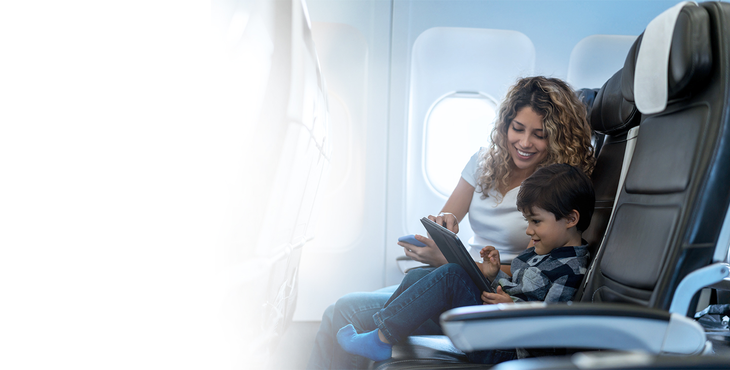 A woman sitting next to her son on a plane is helping him connect his tablet to on-plane wifi