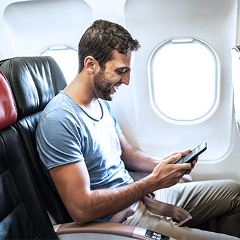 Brown haired man sitting next to a window on the plane using inflight internet on his smartphone