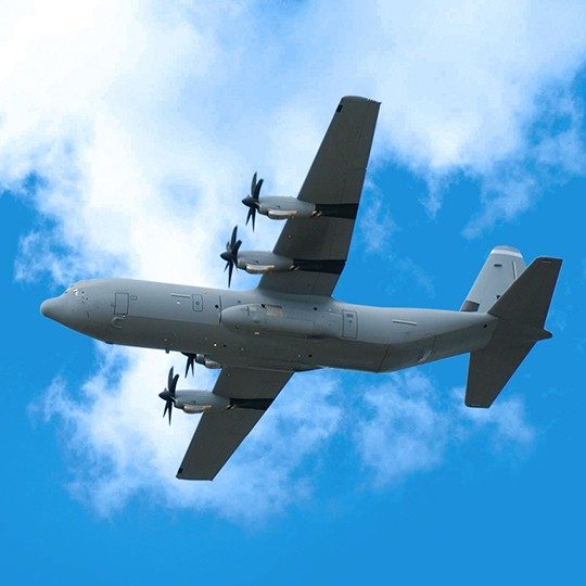 Gray colored military plane flying against a blue sky with clouds