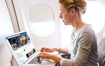 Woman airplane passengers using airplane internet to browse Facebook on her laptop
