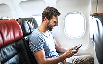 Male passenger sitting near plane window, using airplane internet on his smartphone