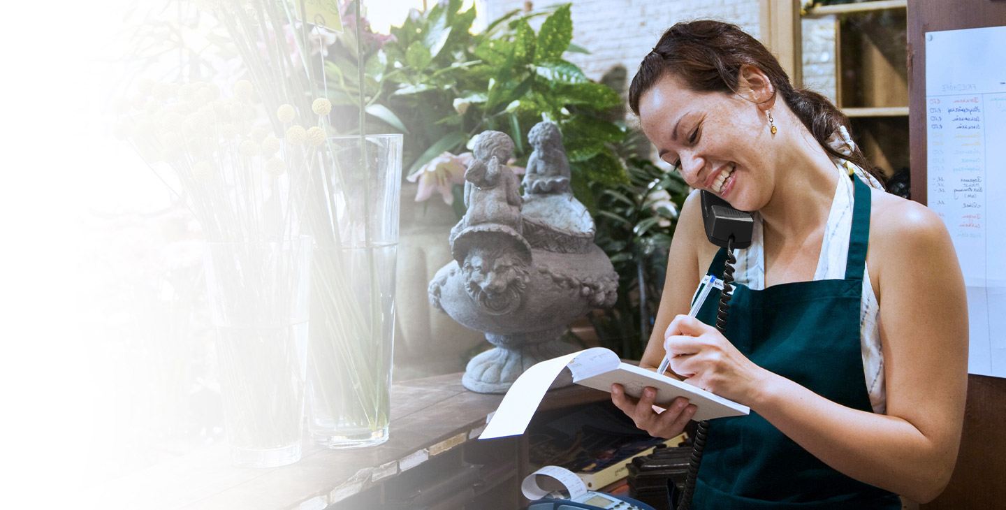 Woman wearing green apron taking an over on the phone using business VoIP