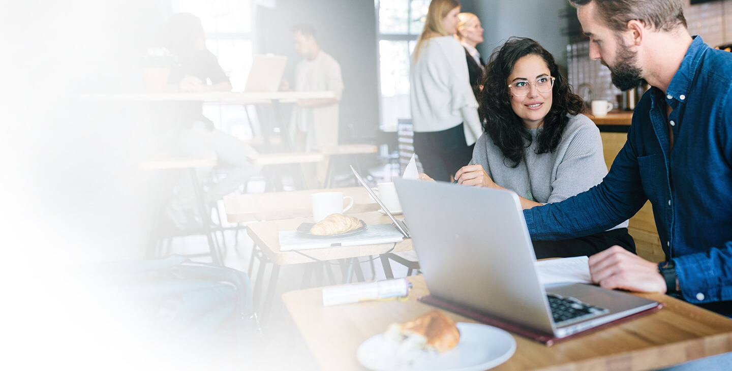 Man and woman customers sitting at a coffee shop using a business hotspot to work from their laptops