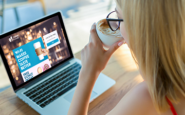 Woman in glasses drinking a coffee looking at a business wifi hotspot login screen on her laptop