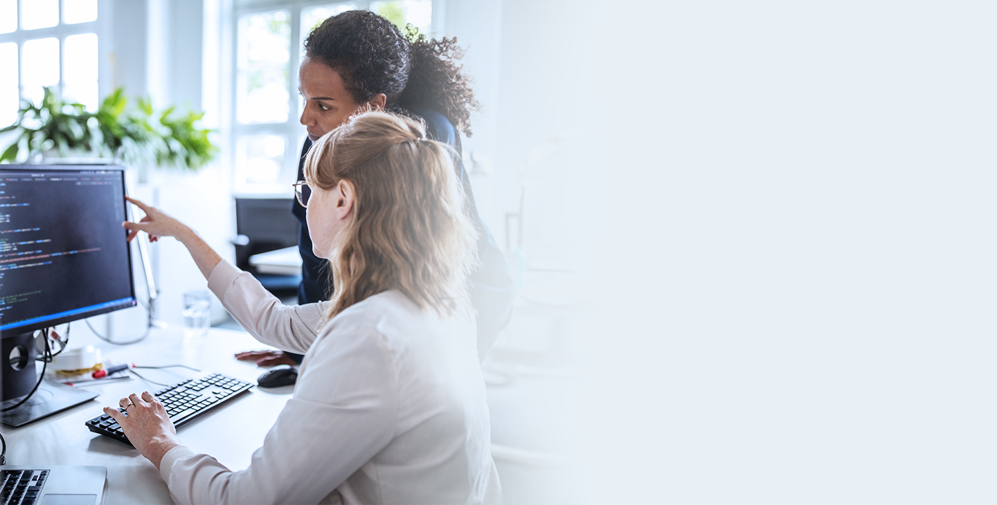 Two business women looking at a desktop monitor utilizing Viasat managed wifi solutions