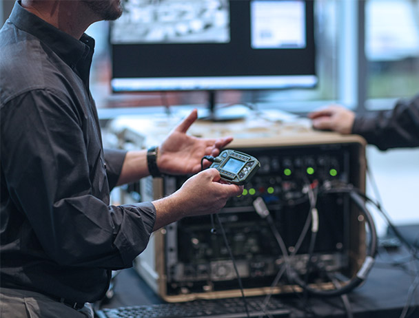 Close-up of of a man in a lab, talking to another Viasat employee, holding a piece of SATCOM equipment