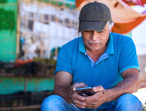 Man wearing a hat and blue polo, sitting outside of a store looking at his smartphone