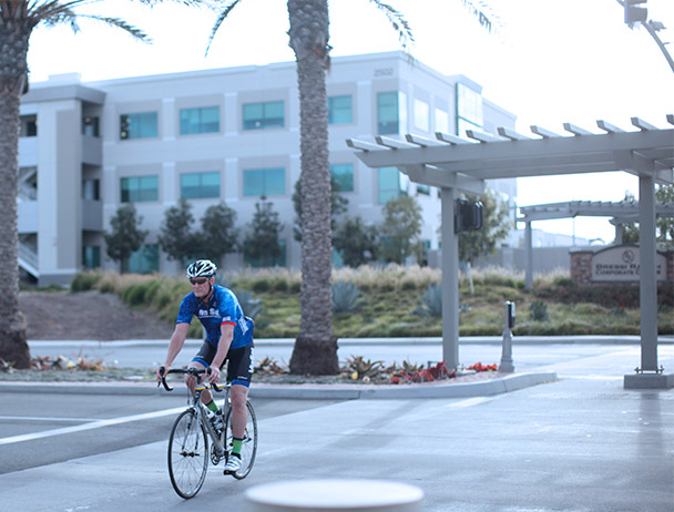 Viasat employee riding his bike across the crosswalk at the corporate Carlsbad campus