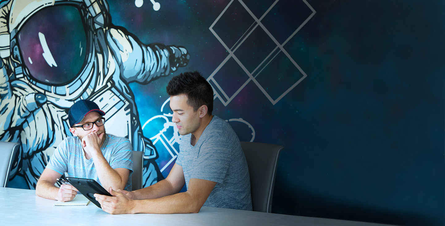 Two male Viasat employees working at a table in front of astronaut wall painting