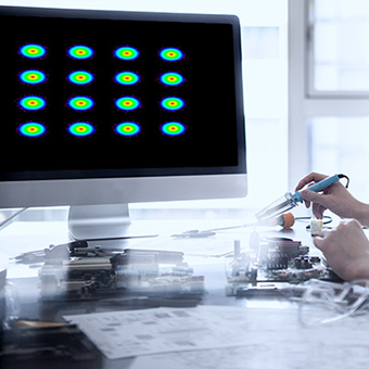 Close-up of a hand holding a tool in front of a monitor with vibrant dots on the screen