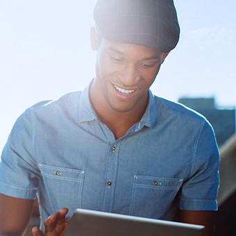 Man wearing a blue button up shirt and a flat cap smiling at a tablet