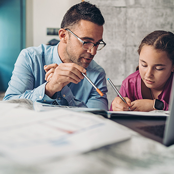 Man sitting at a table with his daughter, helping her with homework