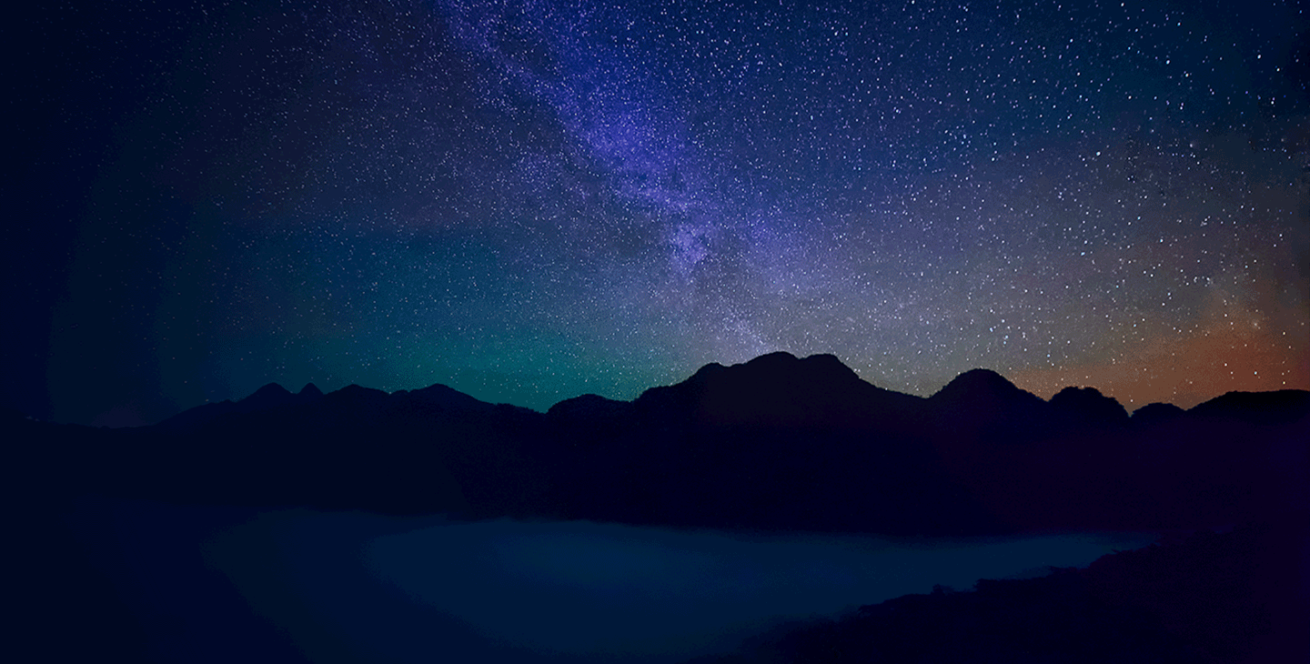 A view of the clear night sky with a silhouetted horizon landscape