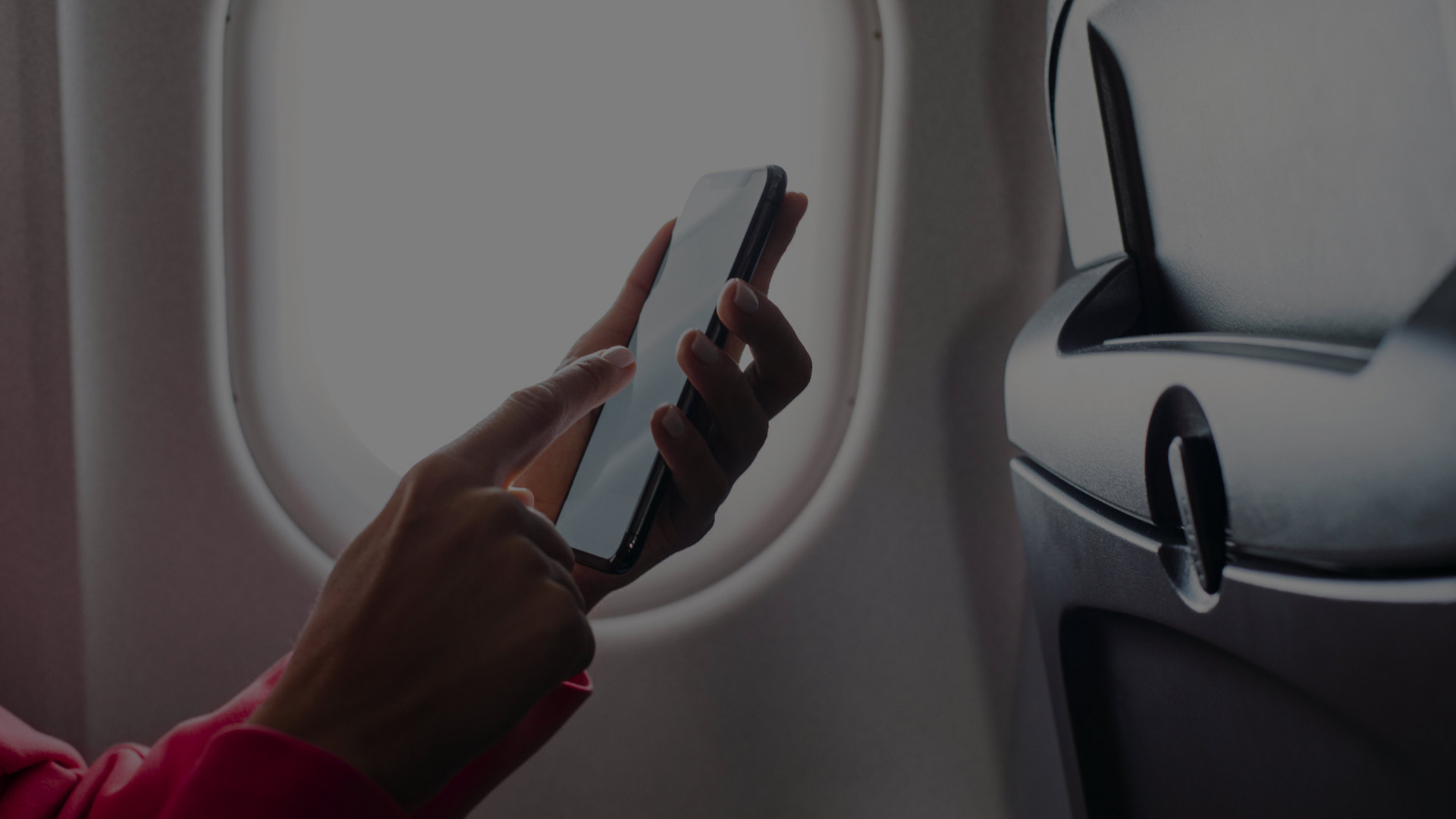 A person uses a mobile phone while sitting next to an airplane window.
