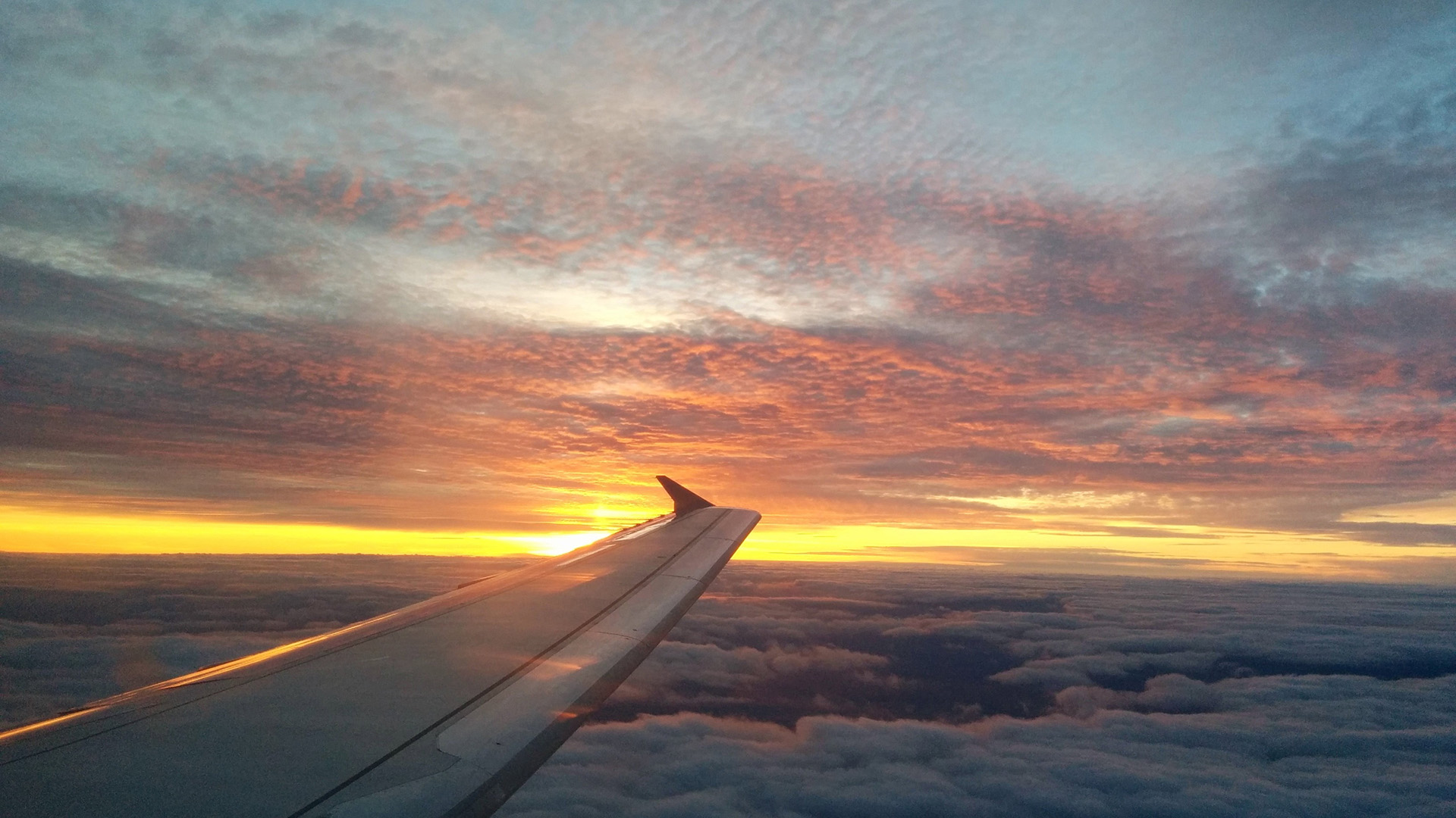 A view of an airplane wing against a cloudy sunset sky.