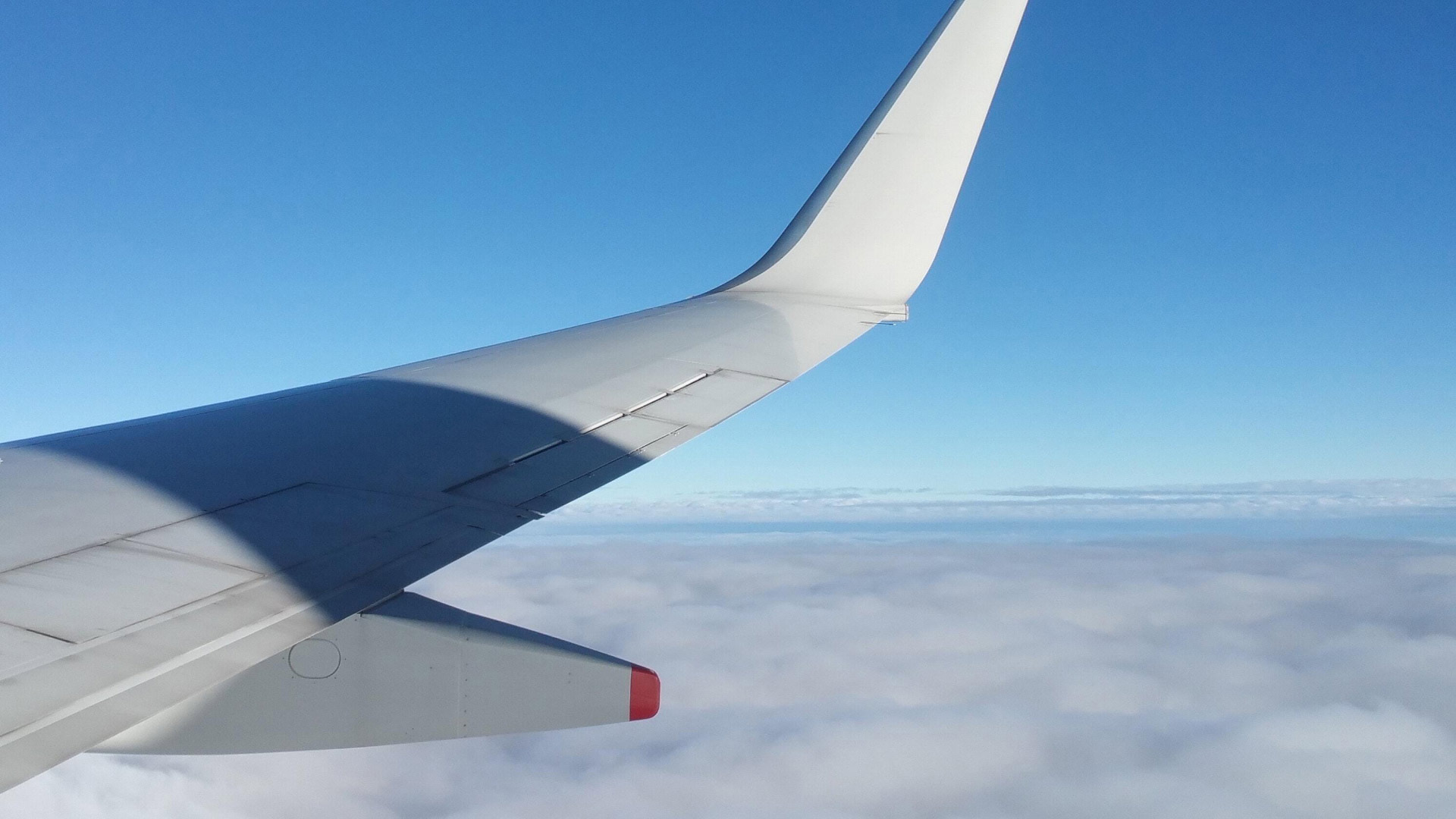 The wing of a private jet above the clouds against a blue sky.