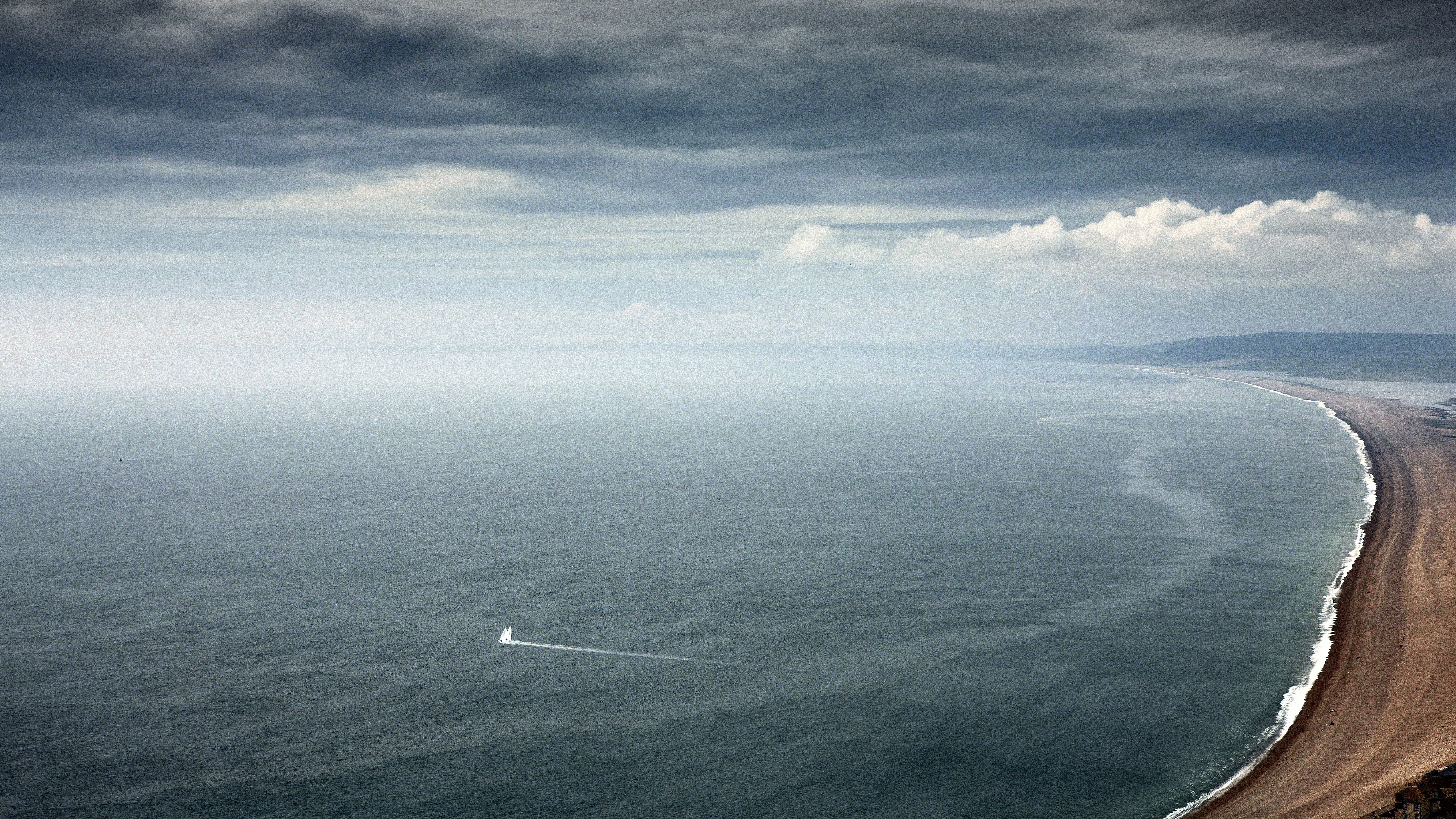An aerial view of a deserted beach with a sailboat heading offshore..