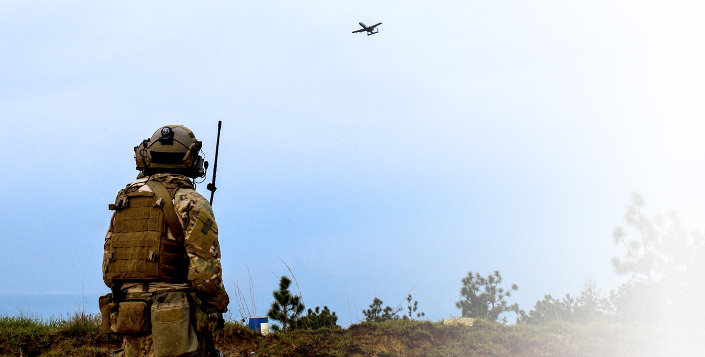 JTAC warfighter  in the field holding a military satcom antenna looking up at an aircraft flying by