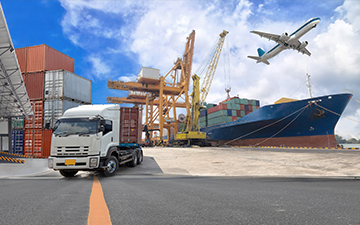 Cargo ship, truck, crane, and airplane flying in the sky