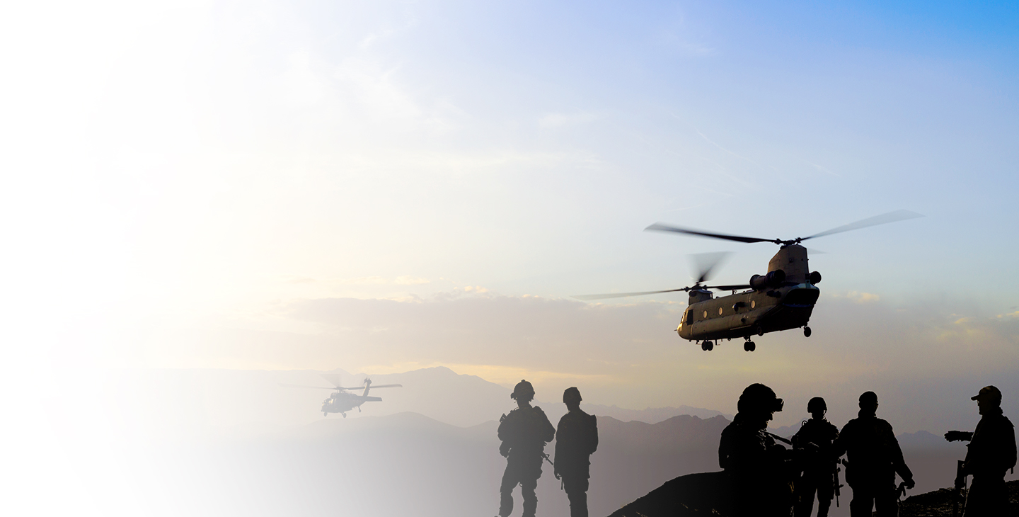 Two helicopters flying over mountains at dusk with warfighters watching