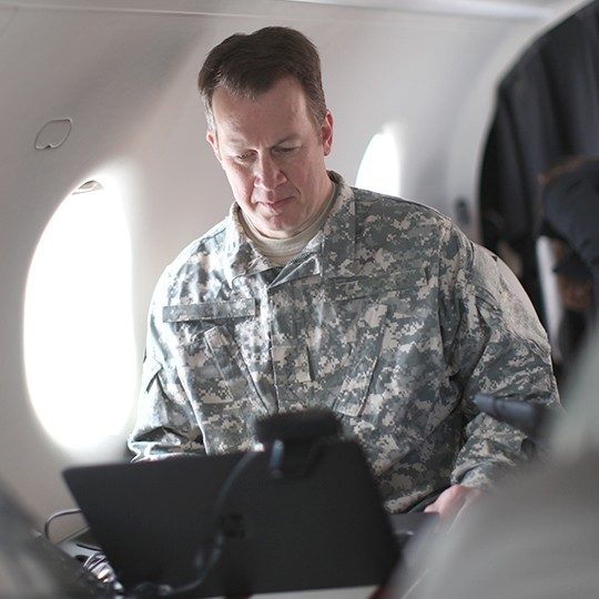 Warfighter connected to his laptop while flying on a government aircraft equipped with dual-band antennas