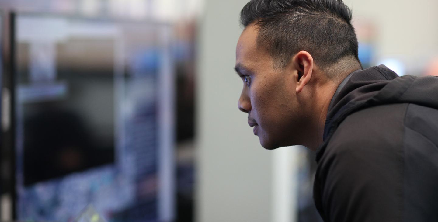 Dark haired man wearing a black jacket looking at Link 16 training on a computer screen