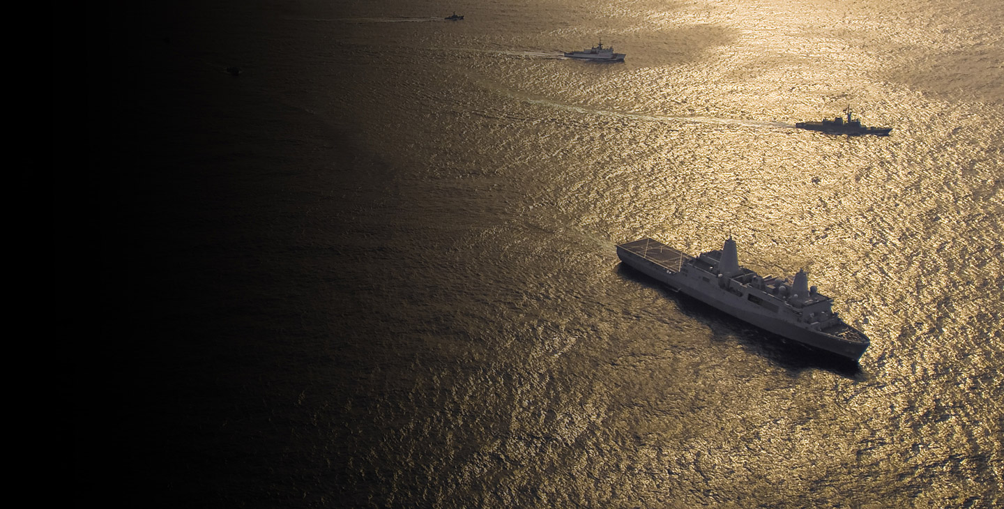 Military fleet of 4 traveling in the ocean at dusk utilizing maritime satellite services