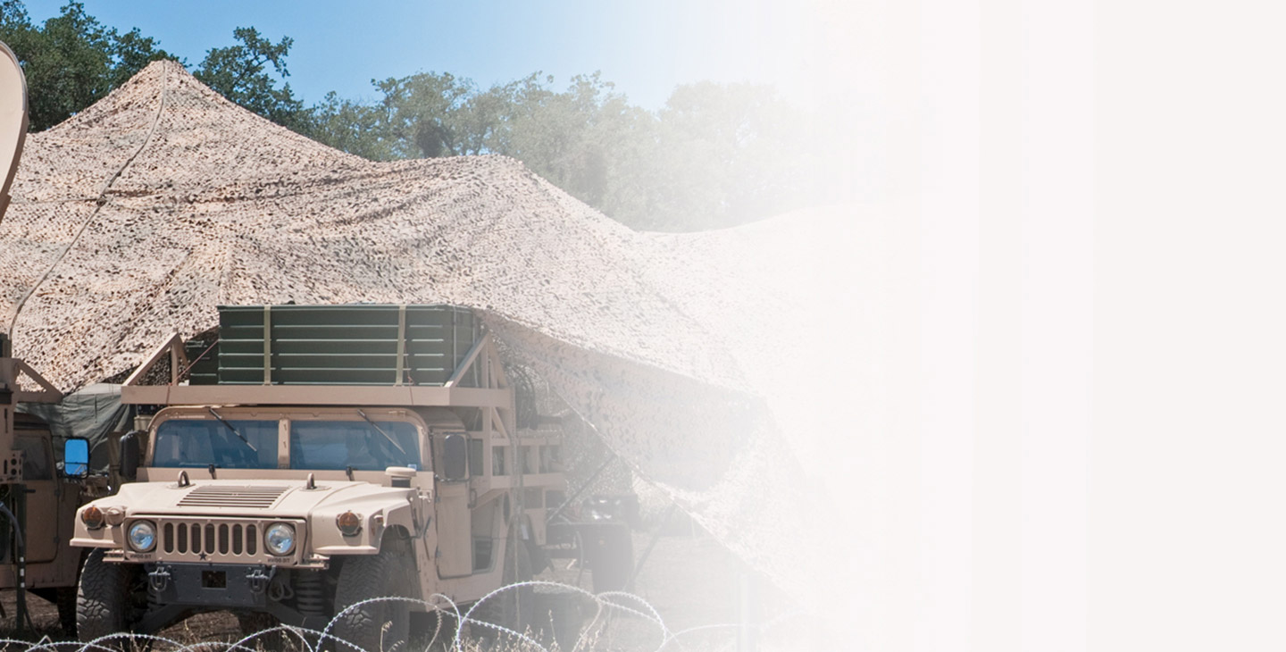 HUMVEE under a camo tent surrounded by barbed-fencing 