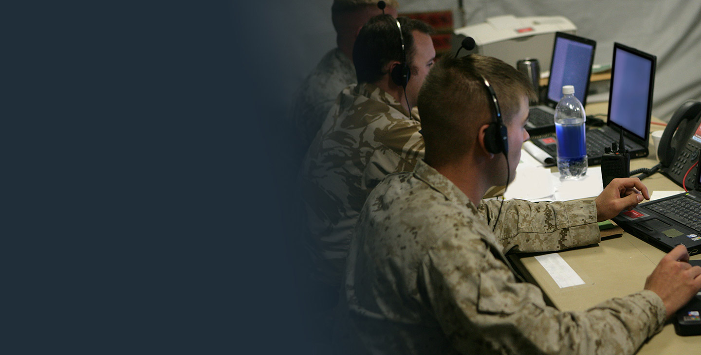 Three male warfighters looking at a laptop in a tactical operations center