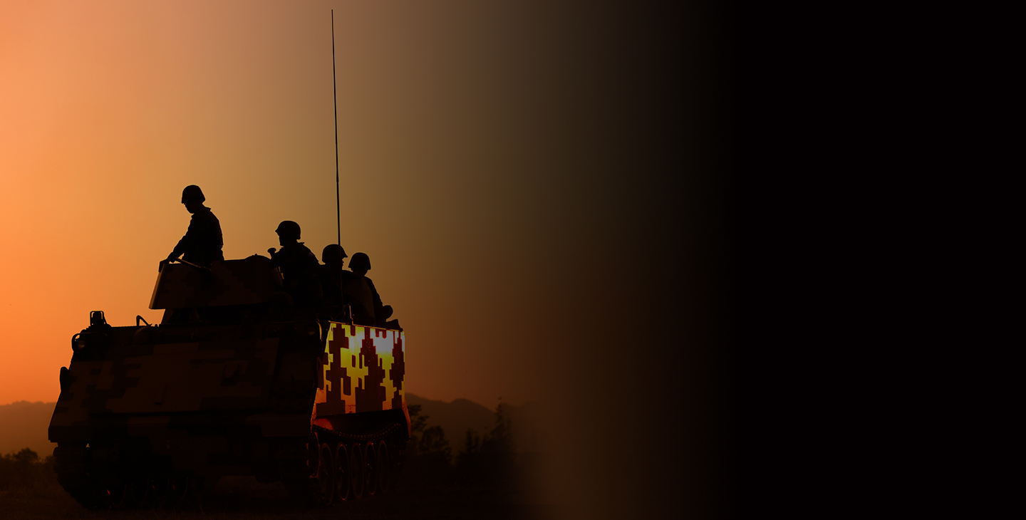 Silhouette of four soliders riding on a tank at dusk