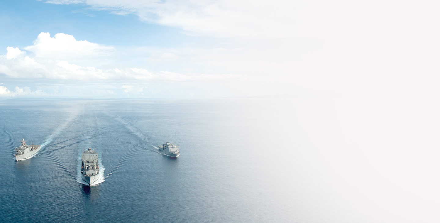 Three navy ships cruising across the open ocean with white clouds in the sky