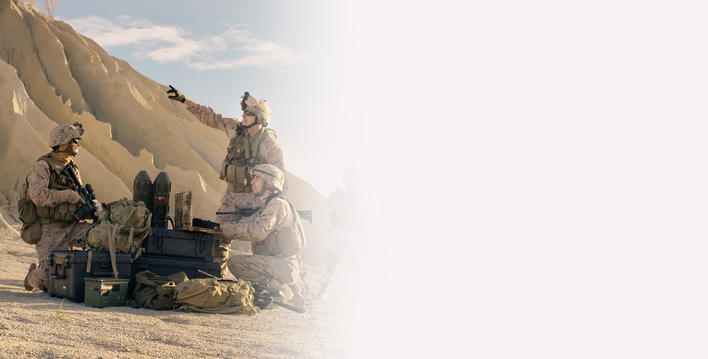 Three soldiers dressed in combat gear talking at the foot of a sand hill next to their combat equipment