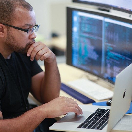 Viasat employee working at a laptop on managed network services next to a larger monitor