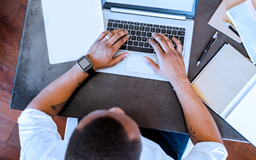 Aerial view of a man wearing a black smartwatch typing on a laptop