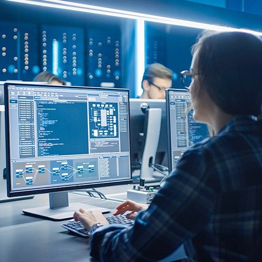 Three employees in a secured network room working on cybersecurity protection on desktop computers