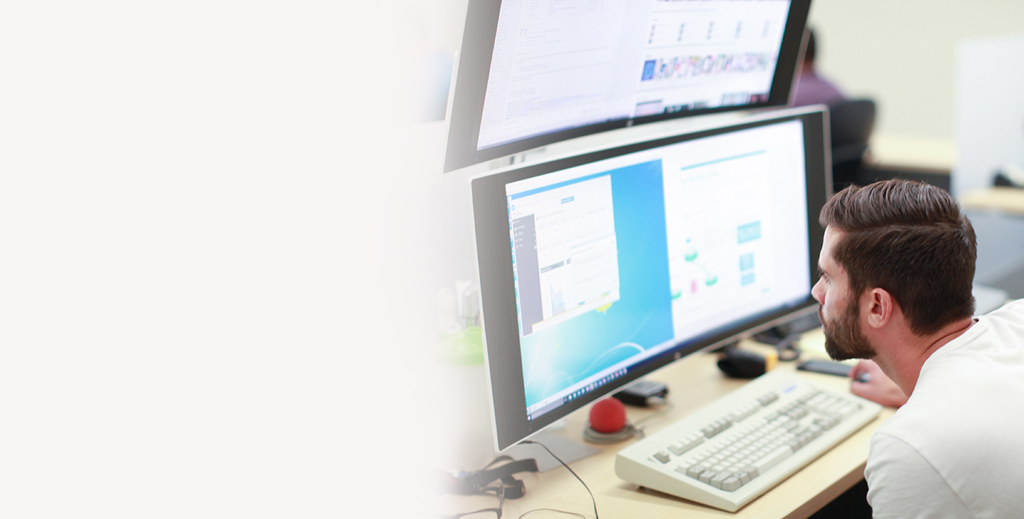 Cybersecurity operations center employee looking intently at two large, stacked monitors on his desk